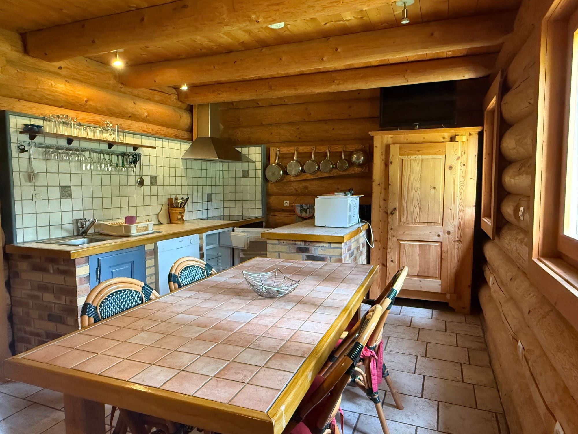 Le séjour en rondins, sa grande table et la cuisine ouverte