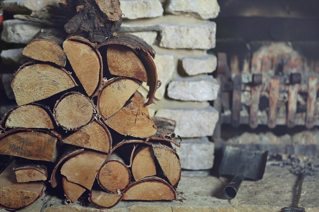 Bûches de bois empilées contre une cheminée en pierre